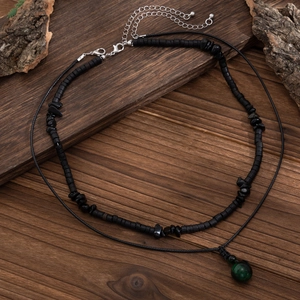 Dettaglio di una collana da uomo a doppio strato con perle nere e un ciondolo verde