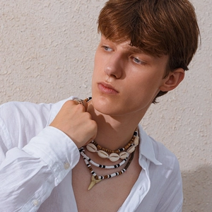 Close-up of men's layered necklace featuring shell beads and a shark tooth pendant