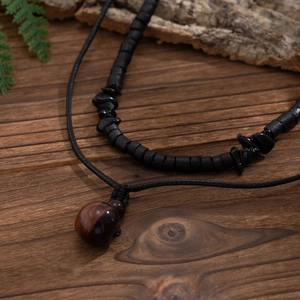 Dettaglio collana di perline con ciondolo occhio di tigre su legno scuro e foglie verdi