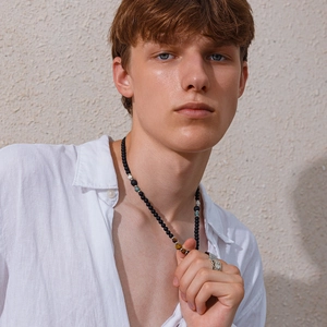 Detail of men's matte black beaded necklace with tiger eye stone and vintage silver rings