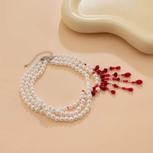 Détail d'un collier de perles à trois rangs avec pampilles rouges sur fond beige doux