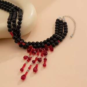 Détail du collier de perles noires multicouche avec glands rouges et fermoir mousqueton