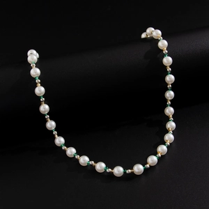 Hip hop pearl necklace with green beads and metallic accents on black display stand