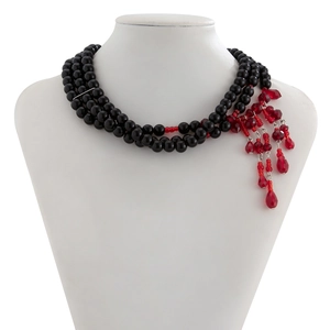 Détail d'un collier à plusieurs rangs avec perles noires et pompons rouges facettés