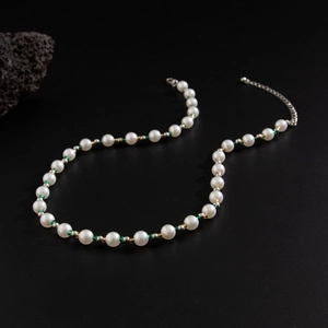 Minimalist pearl necklace with green beads and adjustable clasp on black stone background