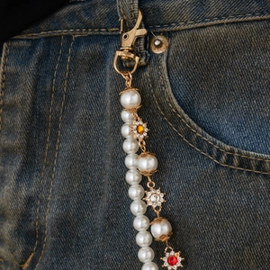 Detailed view of layered pearl trouser chain with colorful floral gemstone charms on denim