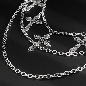 Detail of layered silver cross chains with gothic embossed pendants and retro metal rings