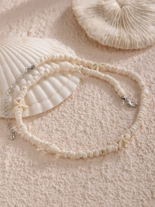 Détail d'un collier de perles avec breloques étoile de mer et coquillage sur corail