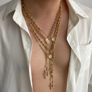 Detail van gelaagde gouden kruiskettingen met religieuze hangers op een wit shirt