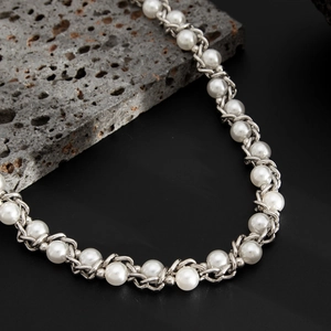 Detail of white pearls interwoven with silver hip-hop style metal chains on a dark stone