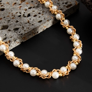 Detailed close-up of white pearls and golden alloy chain on dark textured volcanic rock