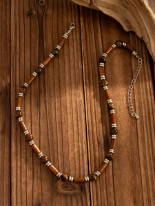 Detail of tiger eye and wood bead necklace with silver lobster clasp on wooden surface