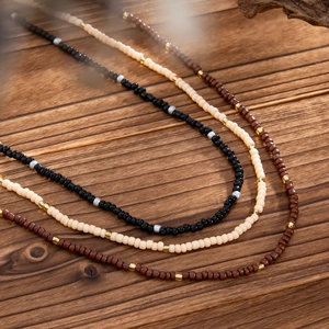 Close-up of handmade beaded necklaces in black, beige, and brown on rustic wood background