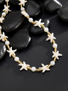 Gros plan d'un collier de perles et d'étoiles de mer sur des galets noirs lisses