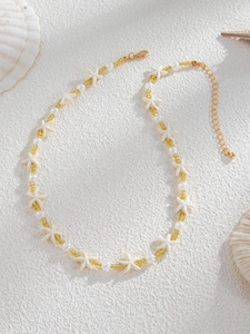 Détail du collier de plage avec étoile de mer blanche, perles et perles jaunes sur sable