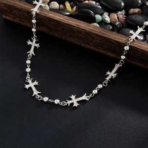 Dettaglio catena gotica argentata con croci di strass su uno sfondo di ciottoli