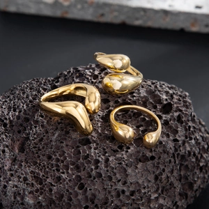 Detailed macro shot of three gold liquid metal teardrop rings on dark volcanic stone