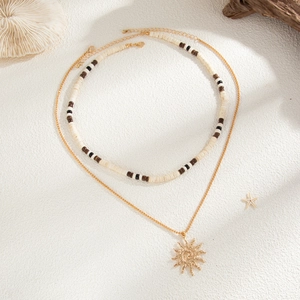 Detail of layered bohemian necklace with wooden beads and a gold sun pendant on sand