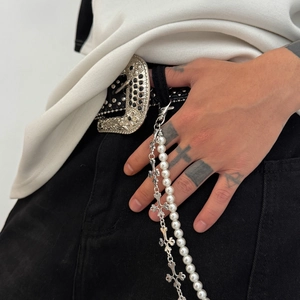 Détail d'une chaîne de pantalon à deux rangs avec croix gothique et perles sur un pantalon