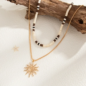 Detail of layered sun pendant necklace on driftwood branch with seaside style props