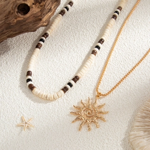 Detail of layered wood bead necklaces with a golden sun pendant on a coastal beach setup