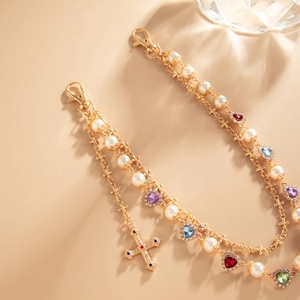 Detail of multilayer gold chain with pearls, colorful heart charms and a cross pendant