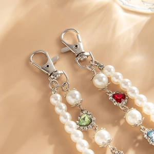 Close-up of pearl chain accessories with heart-shaped colorful gemstones and silver lobster clasp