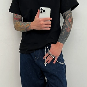 Détail du pendentif croix et perles fantaisie sur une chaîne de pantalon en métal argenté