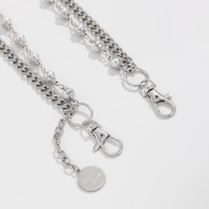Macro detail of multi-layered silver chains with white pearls and a Good Luck tag