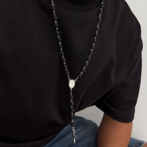 Primo piano della collana di perle nere con croce d'argento e icona religiosa indossata dal modello