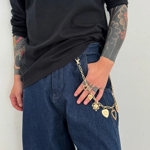 Dettaglio della catena dorata per pantaloni hip-hop con vari pendenti a cuore sui jeans