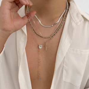 Close-up of layered silver necklaces with cross pendants and herringbone snake chain