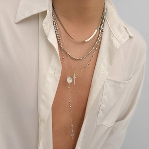 Detail of layered silver necklaces with cross pendants and religious medals on white shirt