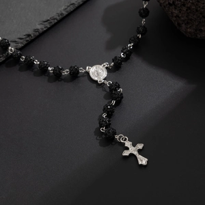 Collana rosario religioso con grani neri e ciondolo a croce d'argento su sfondo di pietra