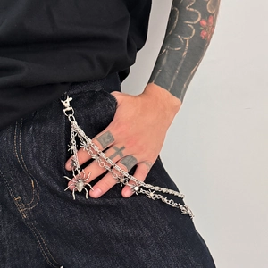 Detail of layered silver metal waist chain featuring multiple spider pendants on jeans