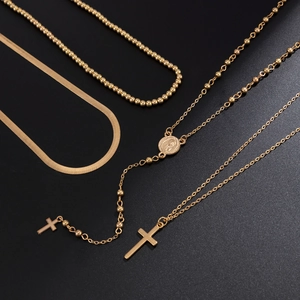 Close-up of gold layered chain set with cross pendant and religious medal on black texture