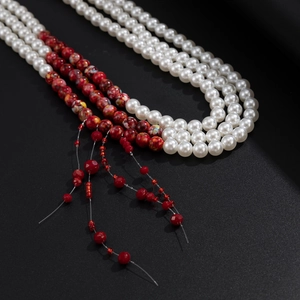 Close-up of beaded pants chain with white faux pearls and red floral fringe tassels
