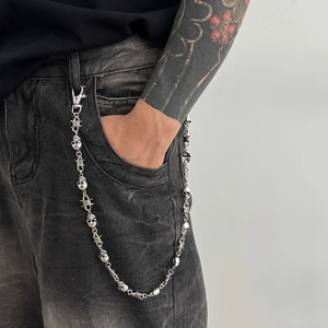 Detail of silver skull punk pant chain with barbed wire links on black denim jeans