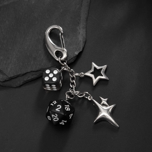 Detail of hip hop style keychain with black d20 dice and silver pentagram on a dark stone background