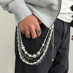 Détail d'un accessoire multicouche en perles et chaînes argentées sur un jean noir