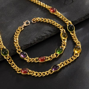 Detail of gold Cuban link set featuring oval multi-colored gemstones on dark stone
