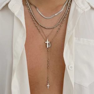 Detail of layered silver necklaces with cross pendants and snake chain on a white shirt