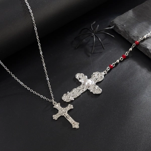Gothic silver cross necklace with red beads and white pearl on a dark stone surface