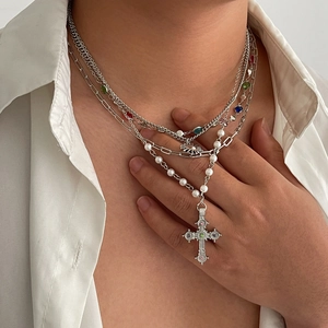 Macro detail of layered silver necklace with pearls, colored gems and vintage cross pendant