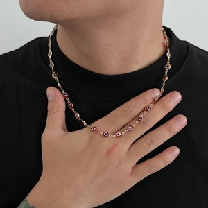 Dettaglio di una collana dorata con perline rosse malocchio su maglietta nera