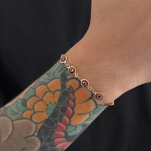 Dettaglio del bracciale a catena dorata con ciondoli occhio del diavolo rosso al polso