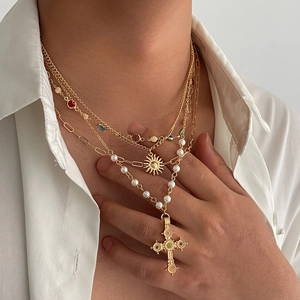 Layered gold necklace featuring cross pendant, sun charm, pearls and colorful gemstones