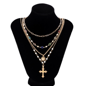 Dettaglio macro della collana dorata multistrato con cristalli colorati, perle e croce