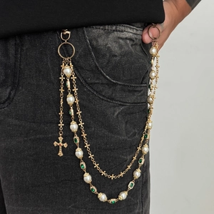 Detail einer mehrlagigen goldenen Hosenkette mit weißen Perlen und Kreuzanhänger auf Denim