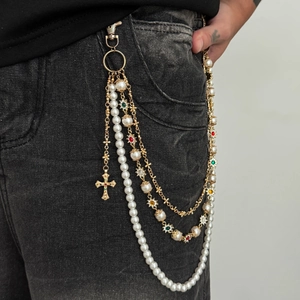 Detail of layered gold pant chain with white pearls and cross pendant on black denim